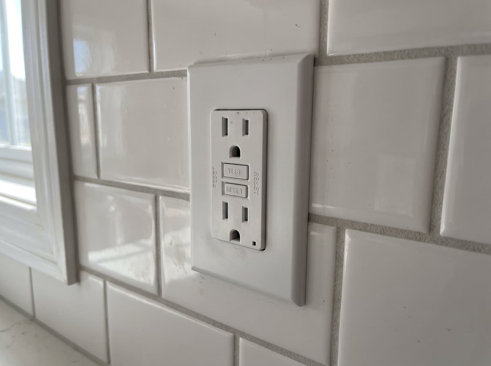 A newly installed white GFCI outlet in a kitchen subway tile backsplash