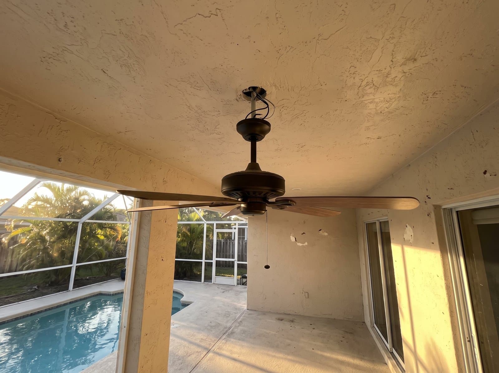 A new outdoor ceiling fan on a covered patio beside a screened pool enclosure