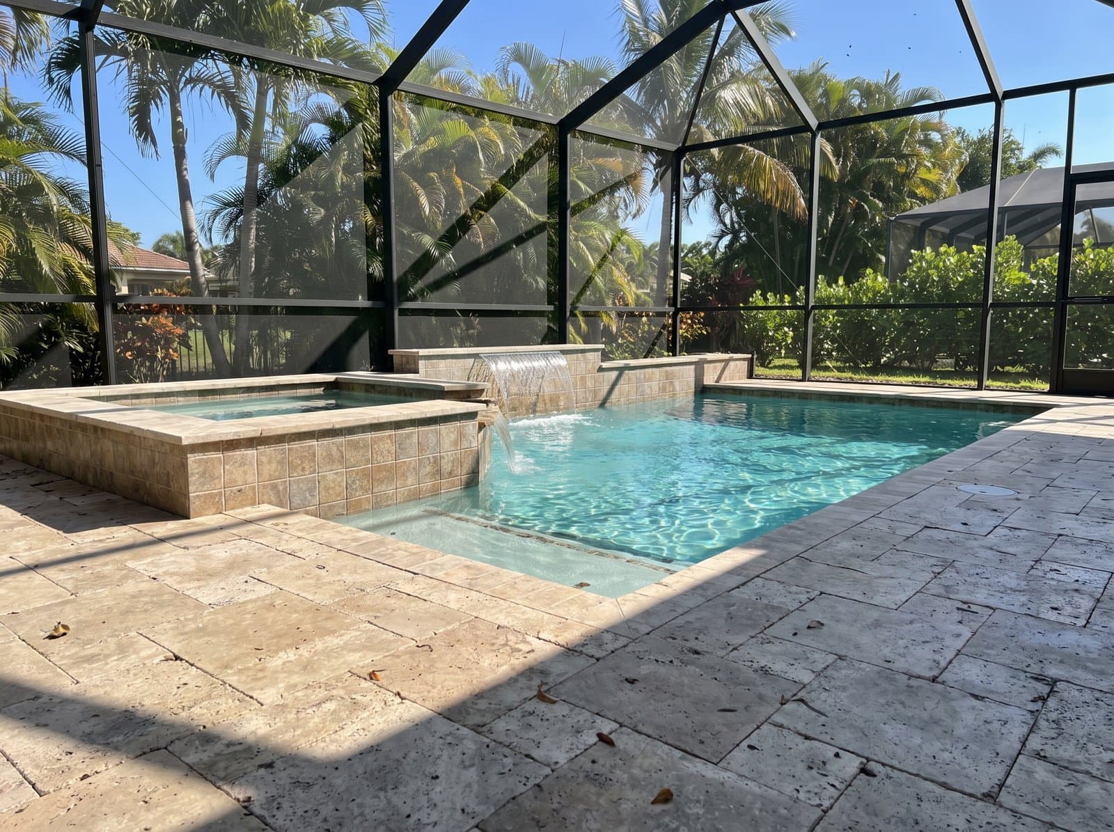 A South Florida pool and raised spa in bright daylight, waterfall running, inside a screened enclosure