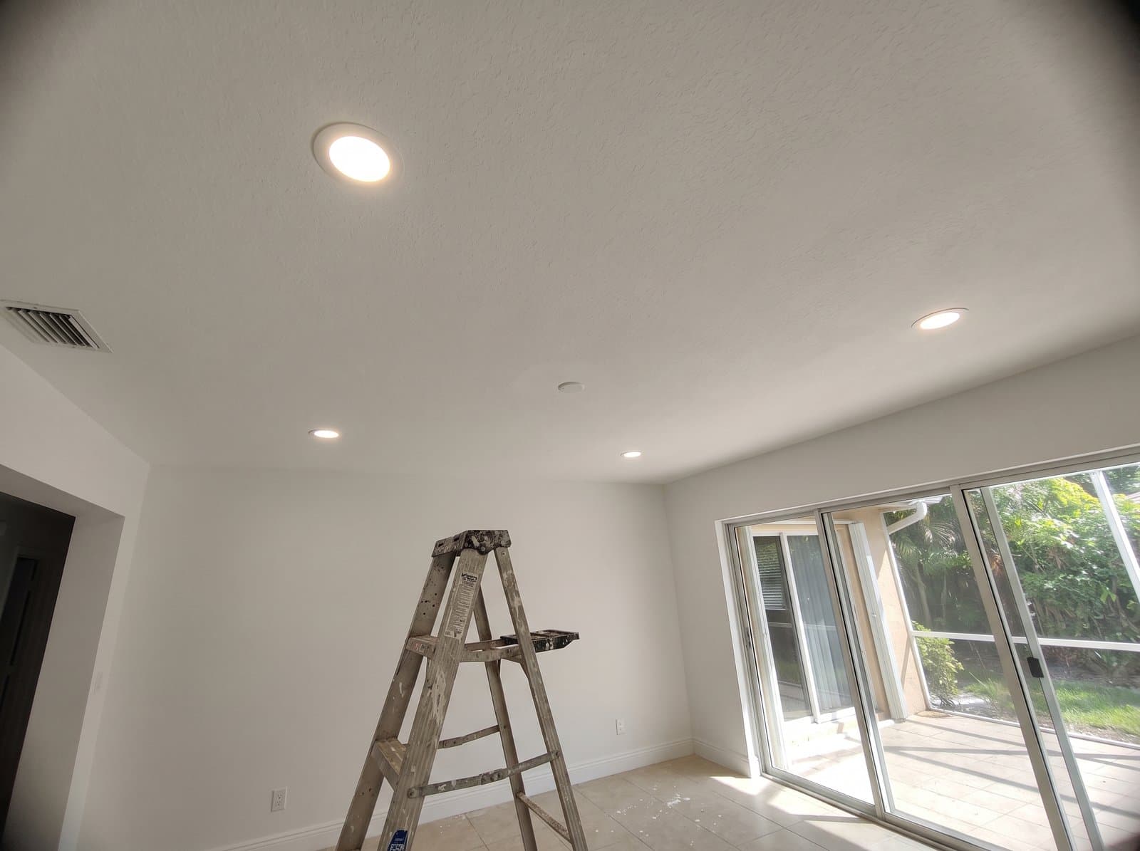 New recessed LED lights glowing in a bright South Florida living room, a step ladder below