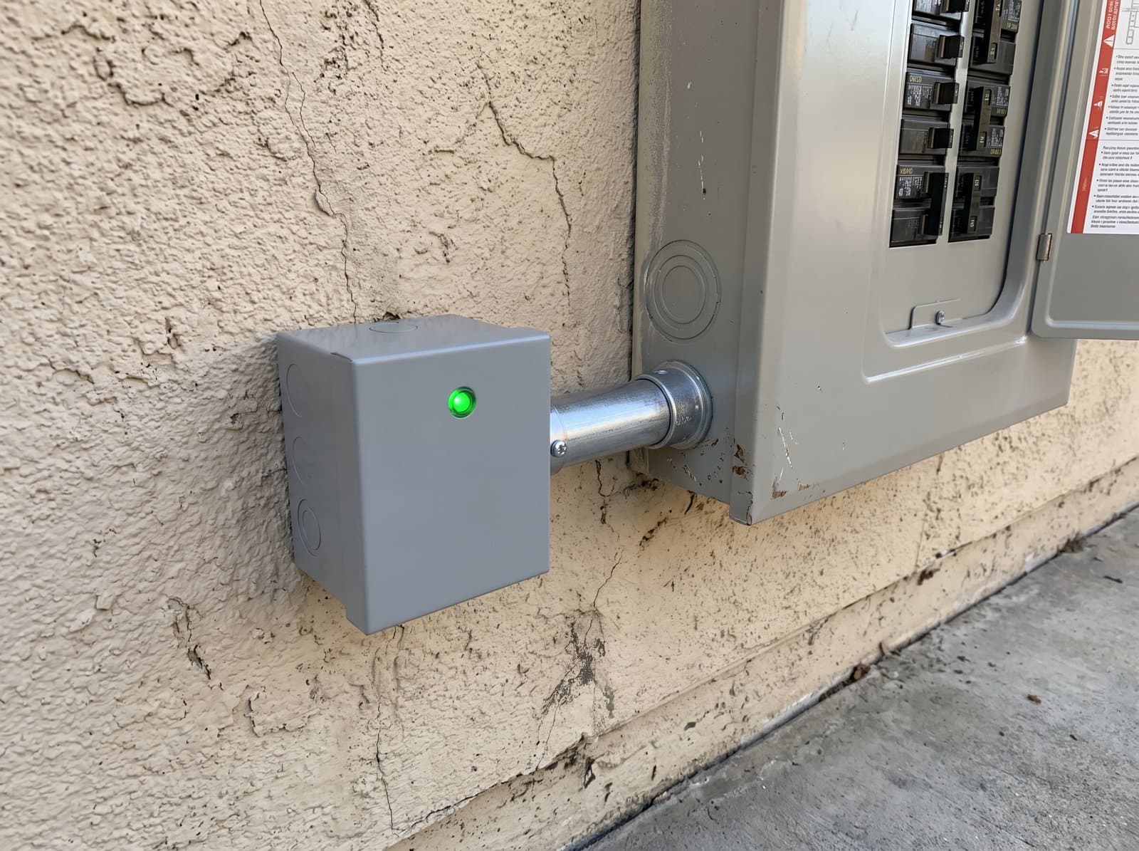 Close up of a whole home surge protective device beside a residential panel, its green status light lit